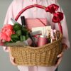 Close-up of woman holding a wicker basket filled with luxury gourmet food hamper gifts against a grey background