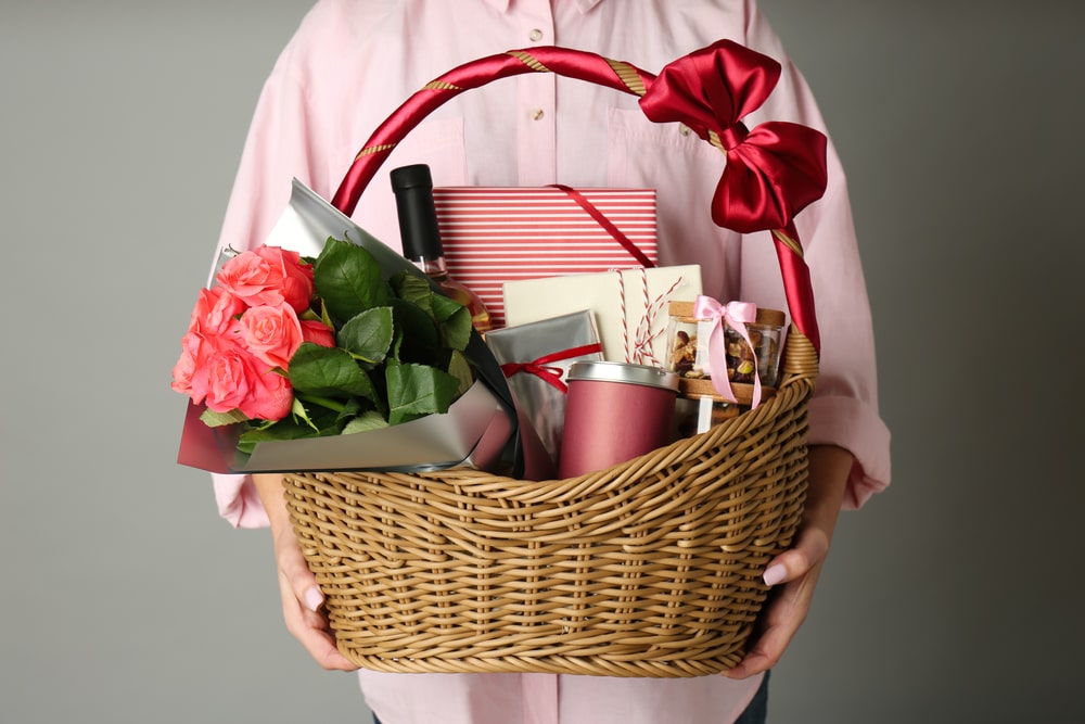 Close-up of woman holding a wicker basket filled with luxury gourmet food hamper gifts against a grey background